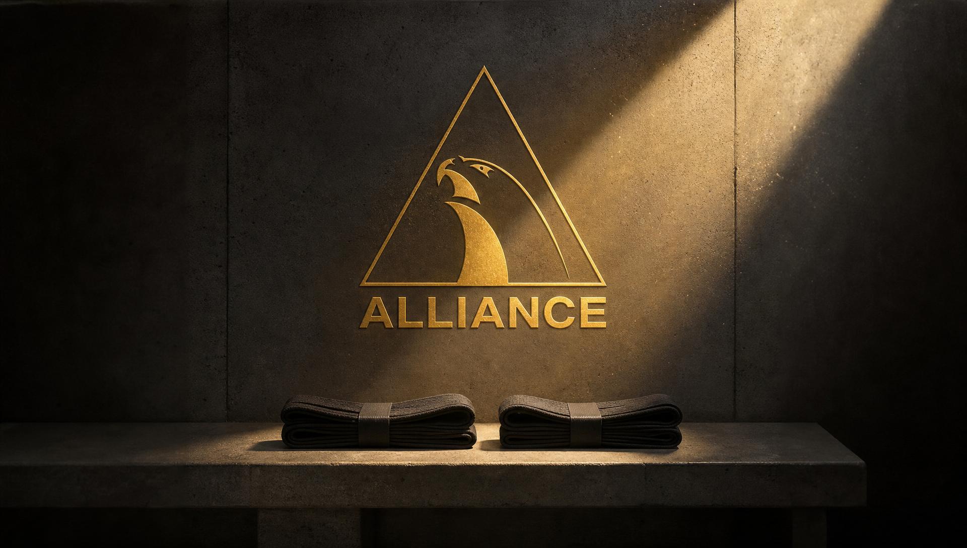 Two black belts on a concrete bench beneath the gold Alliance Jiu-Jitsu logo